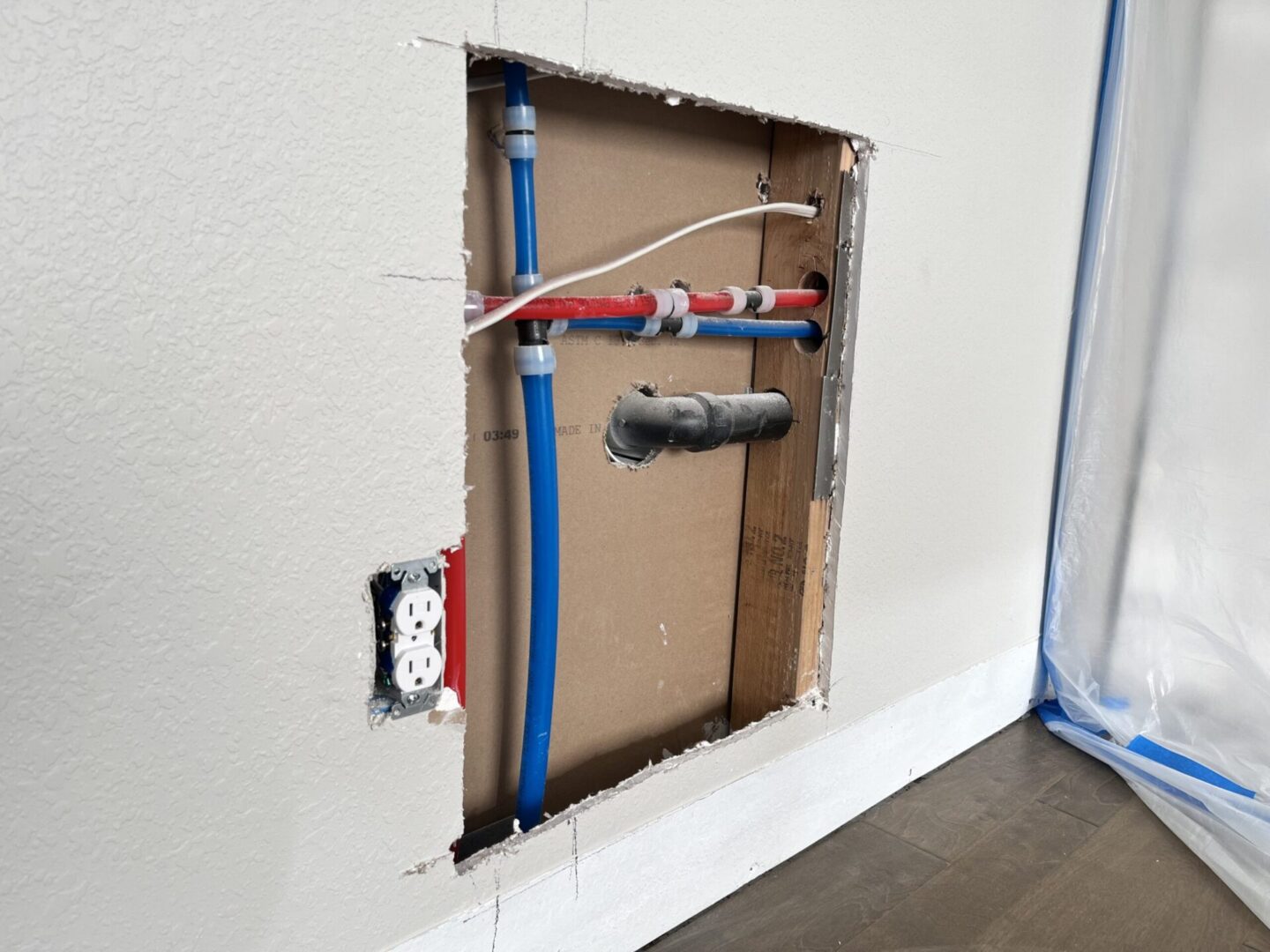 Wall cutout exposing plumbing and electrical outlet.