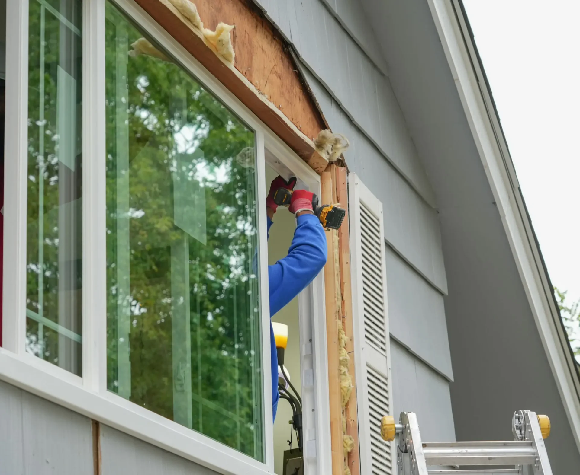 Person installing window frame from ladder.