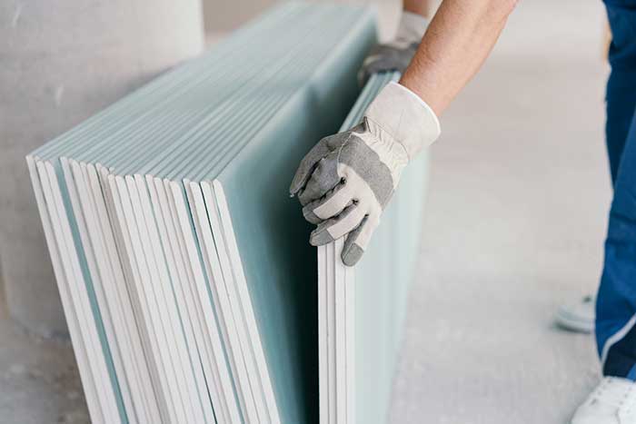 Person handling stack of drywall sheets.