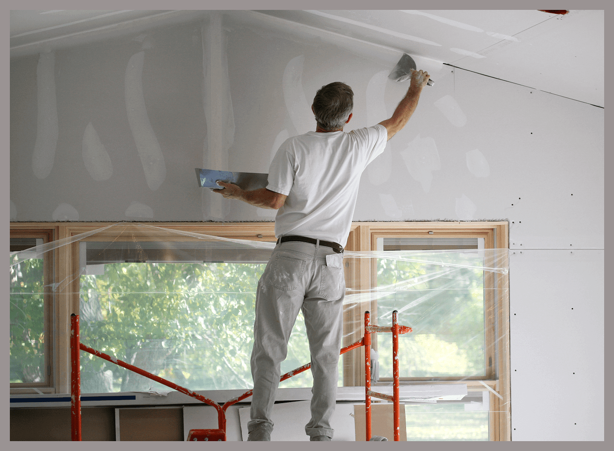 Person plastering a wall on scaffolding.