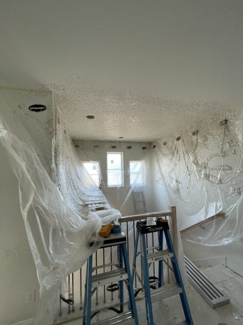 Room under renovation with ladders and plastic sheets.