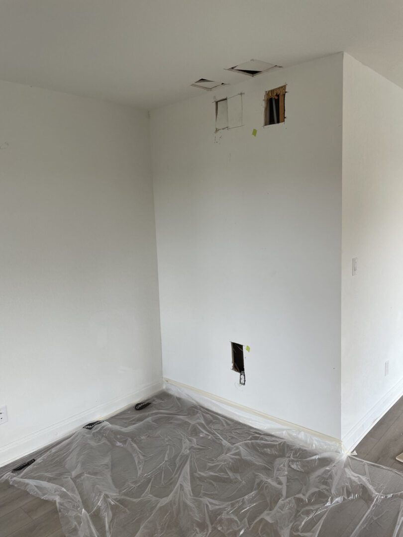 Wall with holes, plastic sheet on floor.