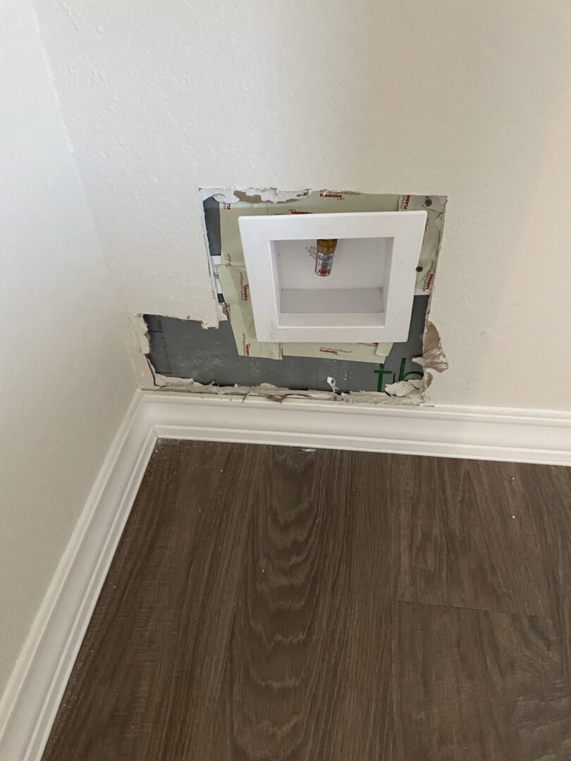 Damaged wall with exposed plumbing pipe.