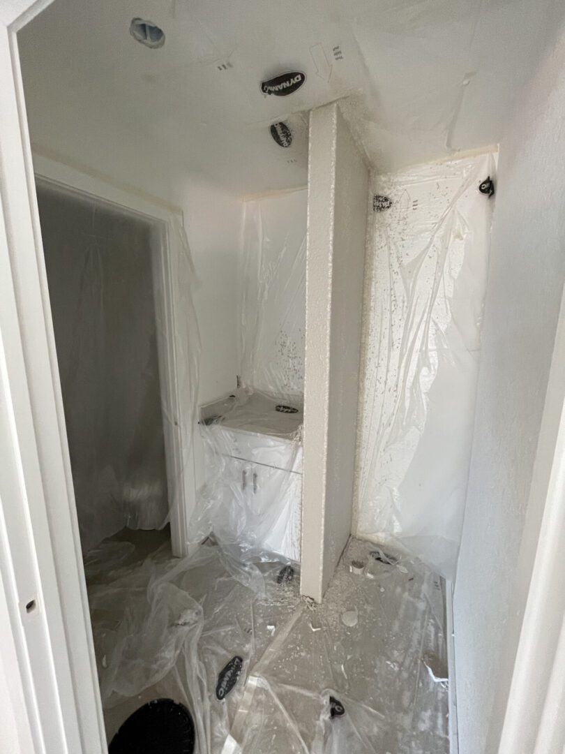 Bathroom under renovation with protective plastic sheets.