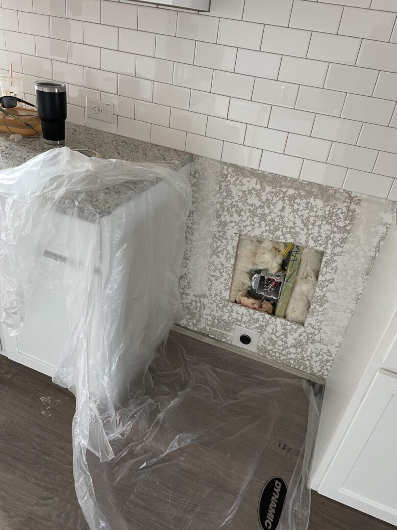 Kitchen wall under repair with plastic covering.